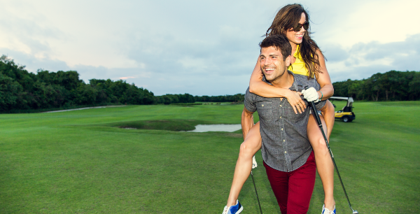 A woman gets a piggyback ride by her boyfriend or husband on a golf course.