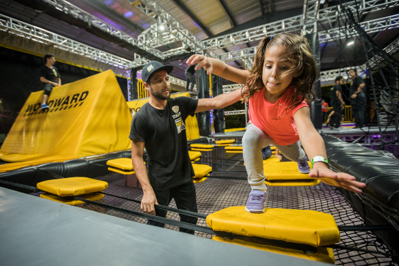 A little girl jumps from a floating disc in an obstacle course called WreckTangle with the help of a Woodward Riviera Maya staff member.