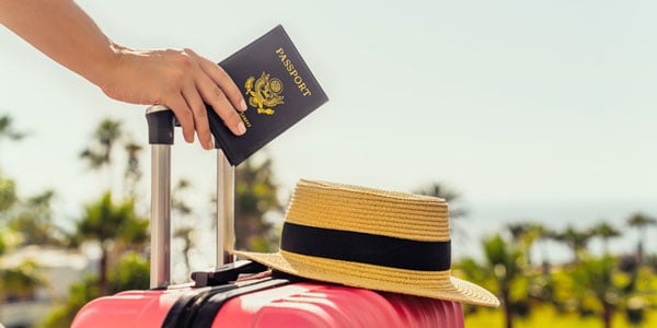 Person holding passport with suitcase and hat